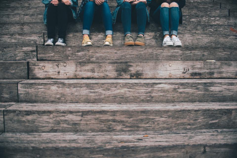 four people sitting on steps. You can view their legs and shoes. They are wearing dark jeans and runners.