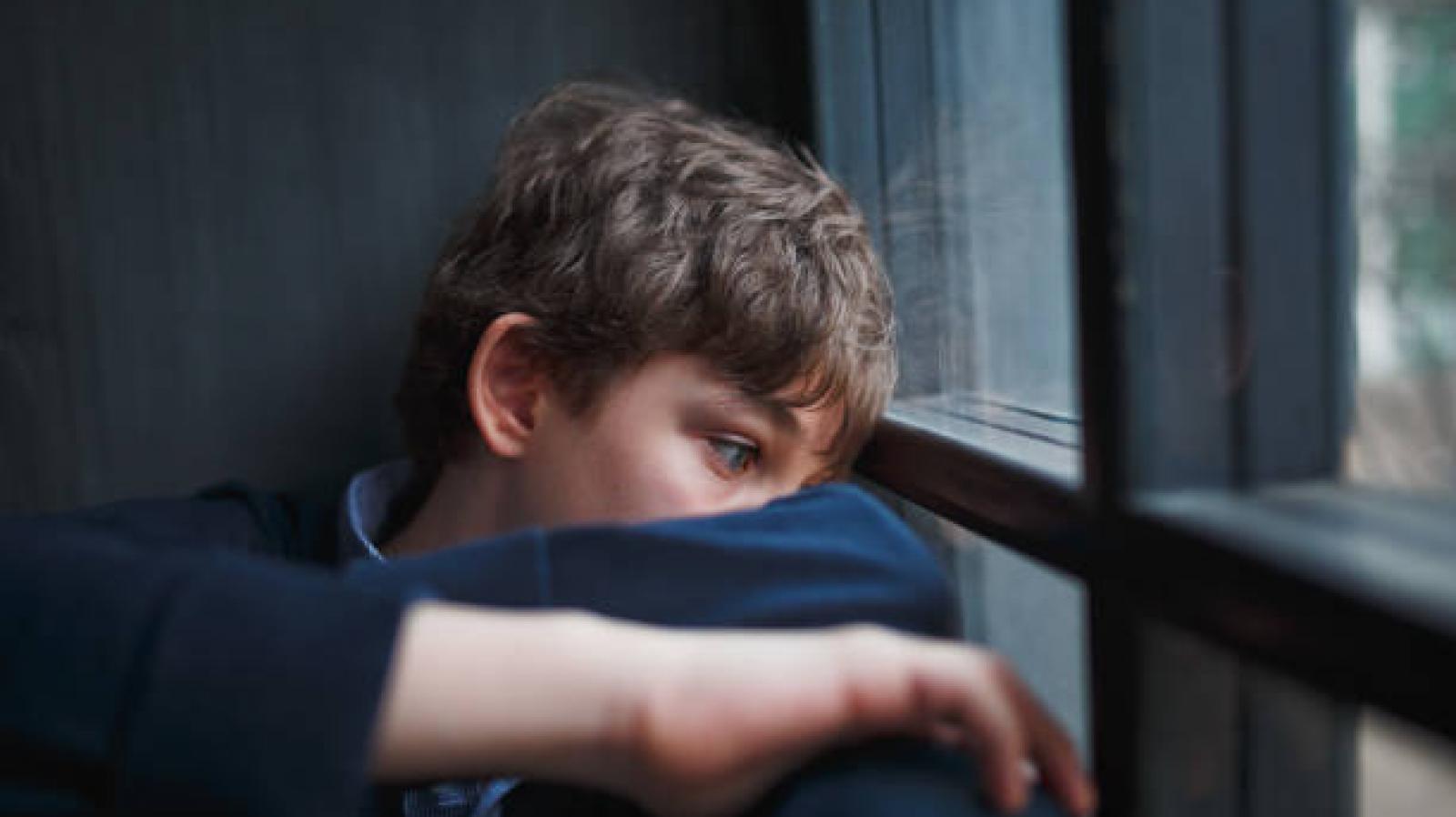 A young boy looks sad whilst looking out a window