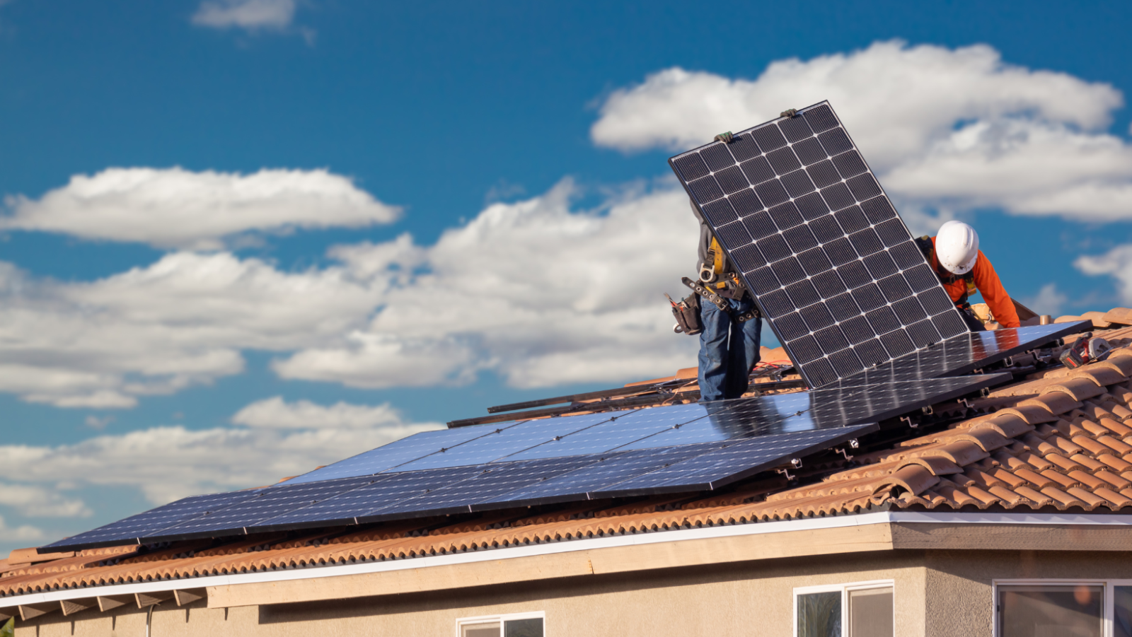 Two workers installing solar panels on the roof of a home