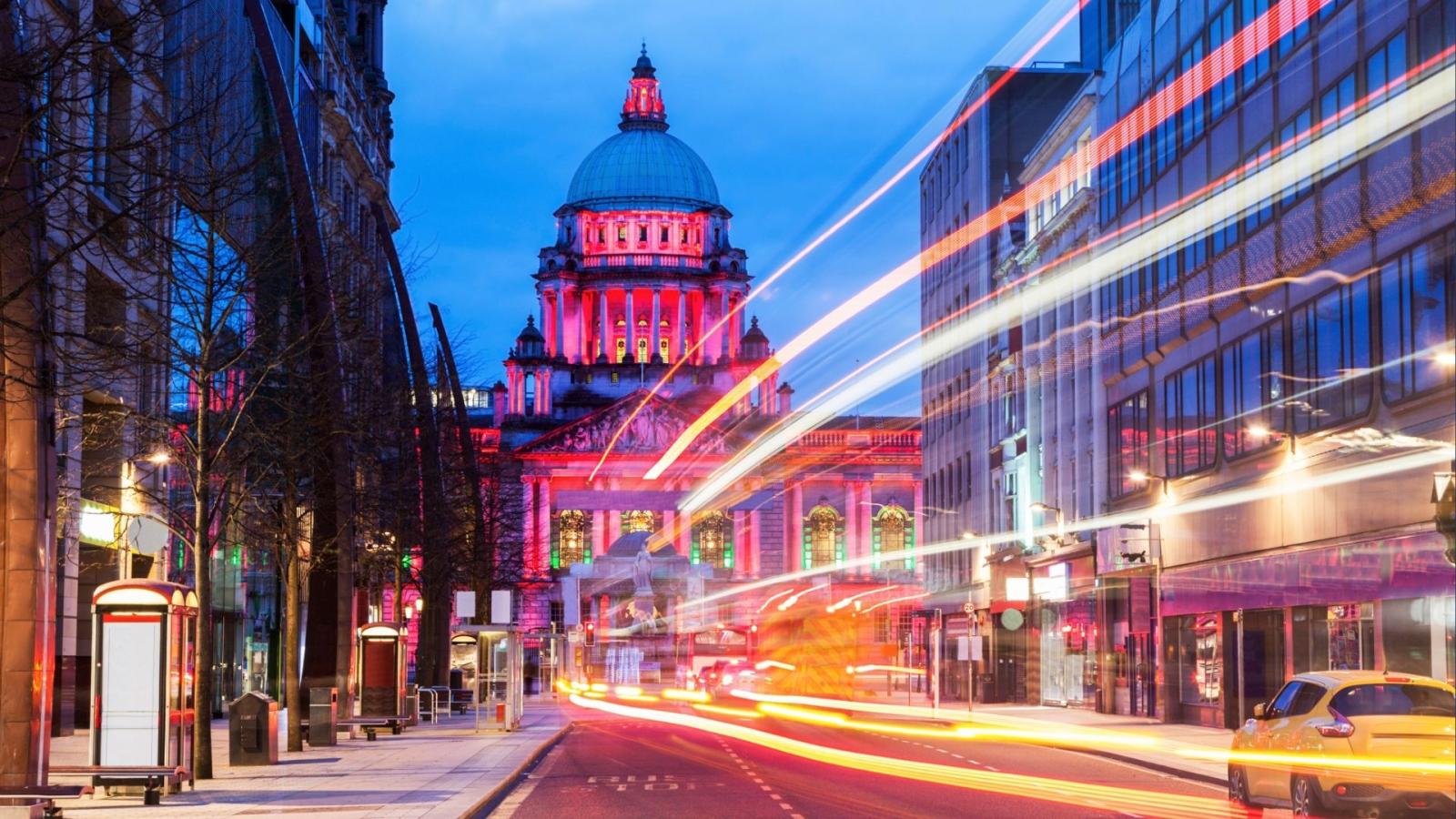 A bustling Belfast street featuring a prominent building in the background, showcasing urban life and architecture.